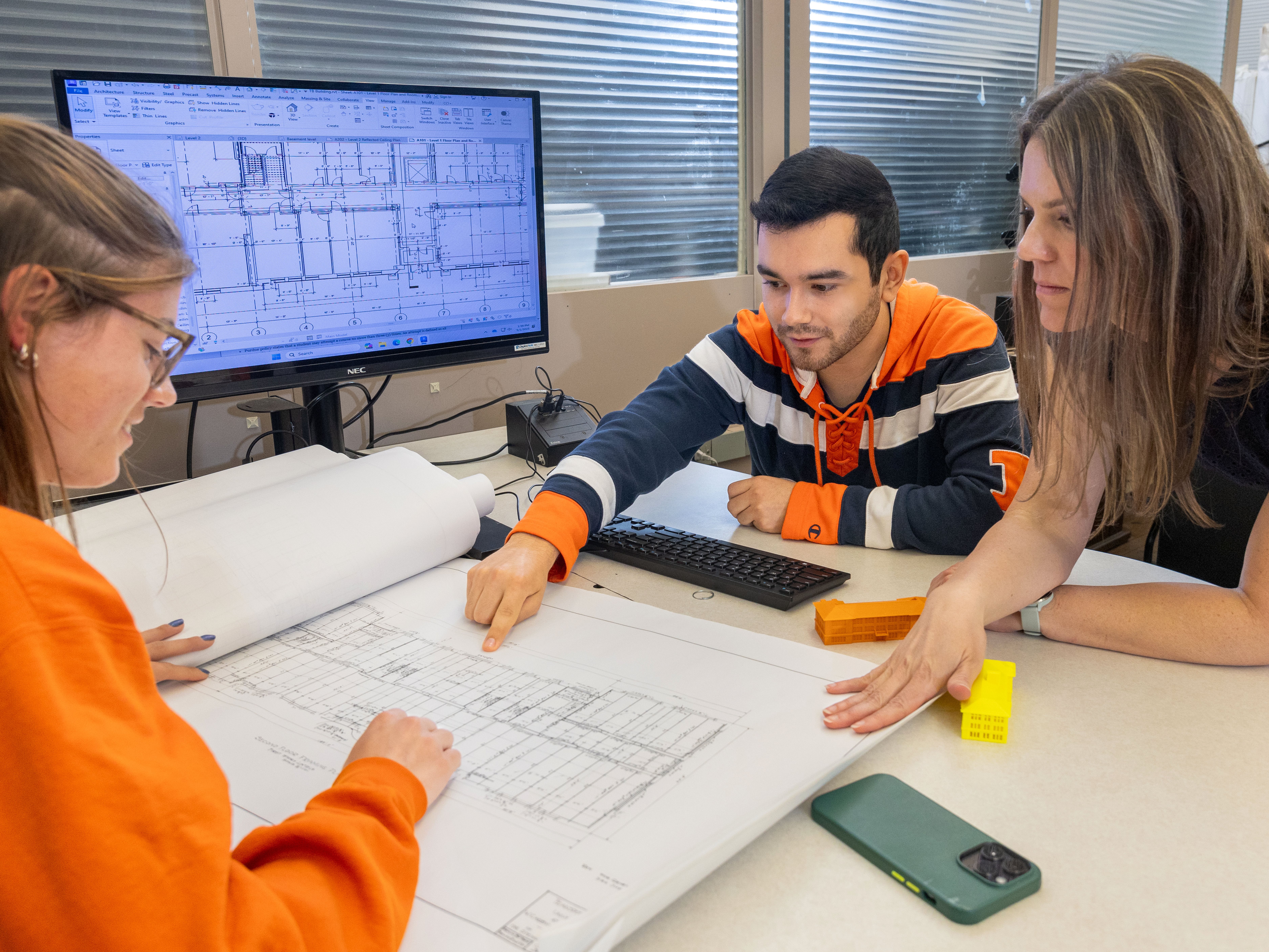 professor molly goldstein sitting at a table with two students who are pointing at building plans