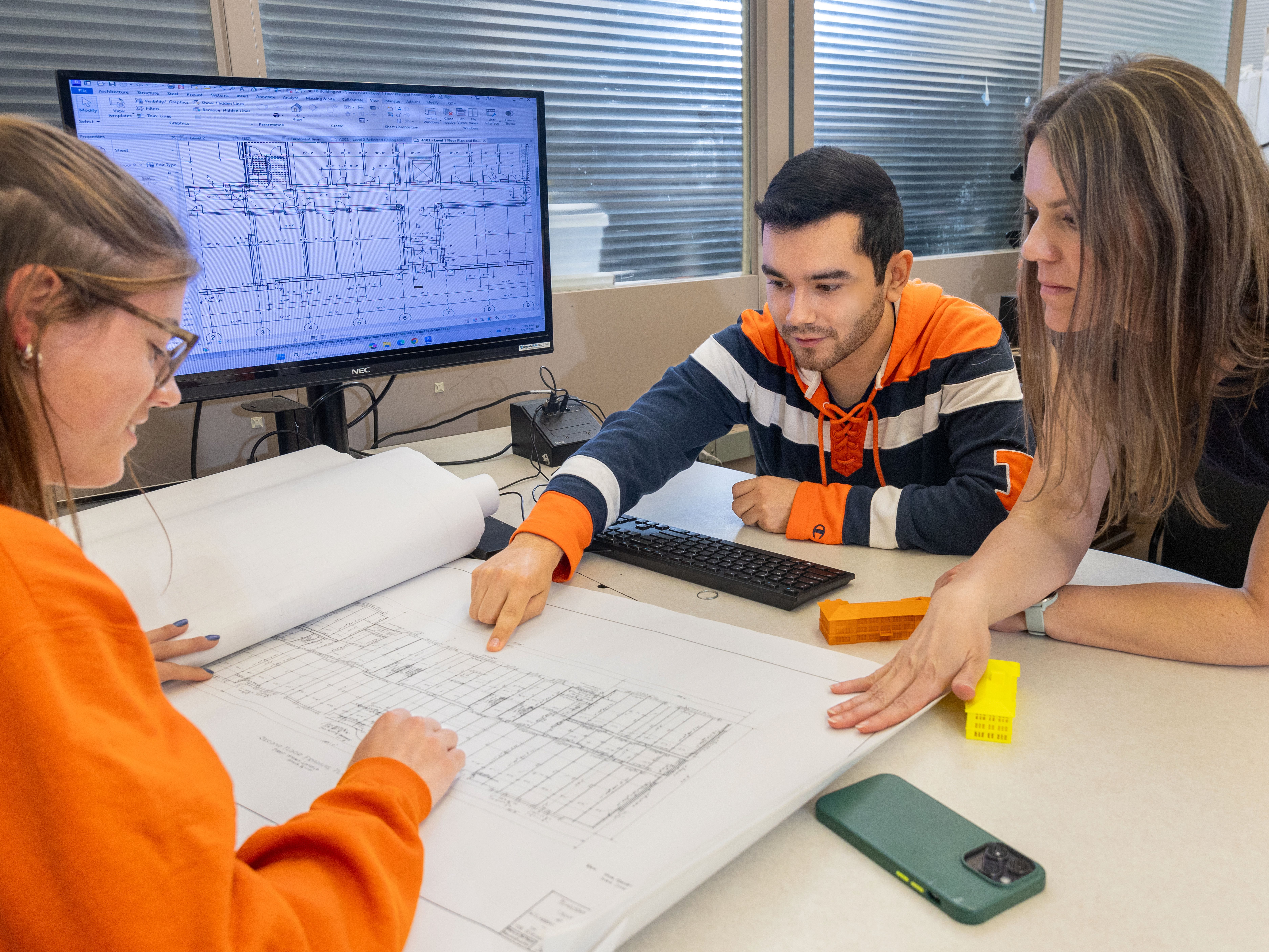 professor molly goldstein sitting at a table with two students who are pointing at building plans