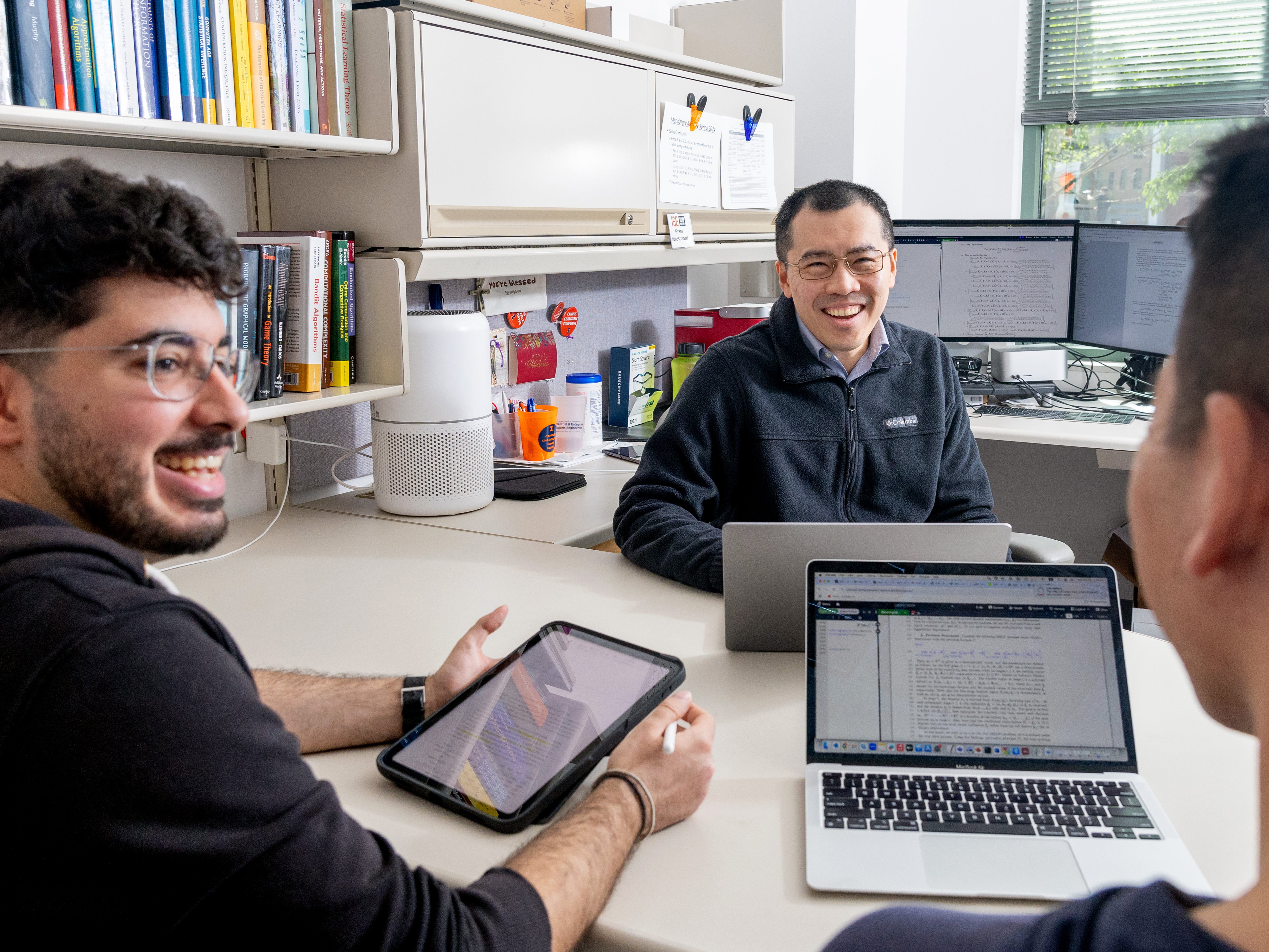 two graduate students sitting with professor grani hanasusanto smiling.
