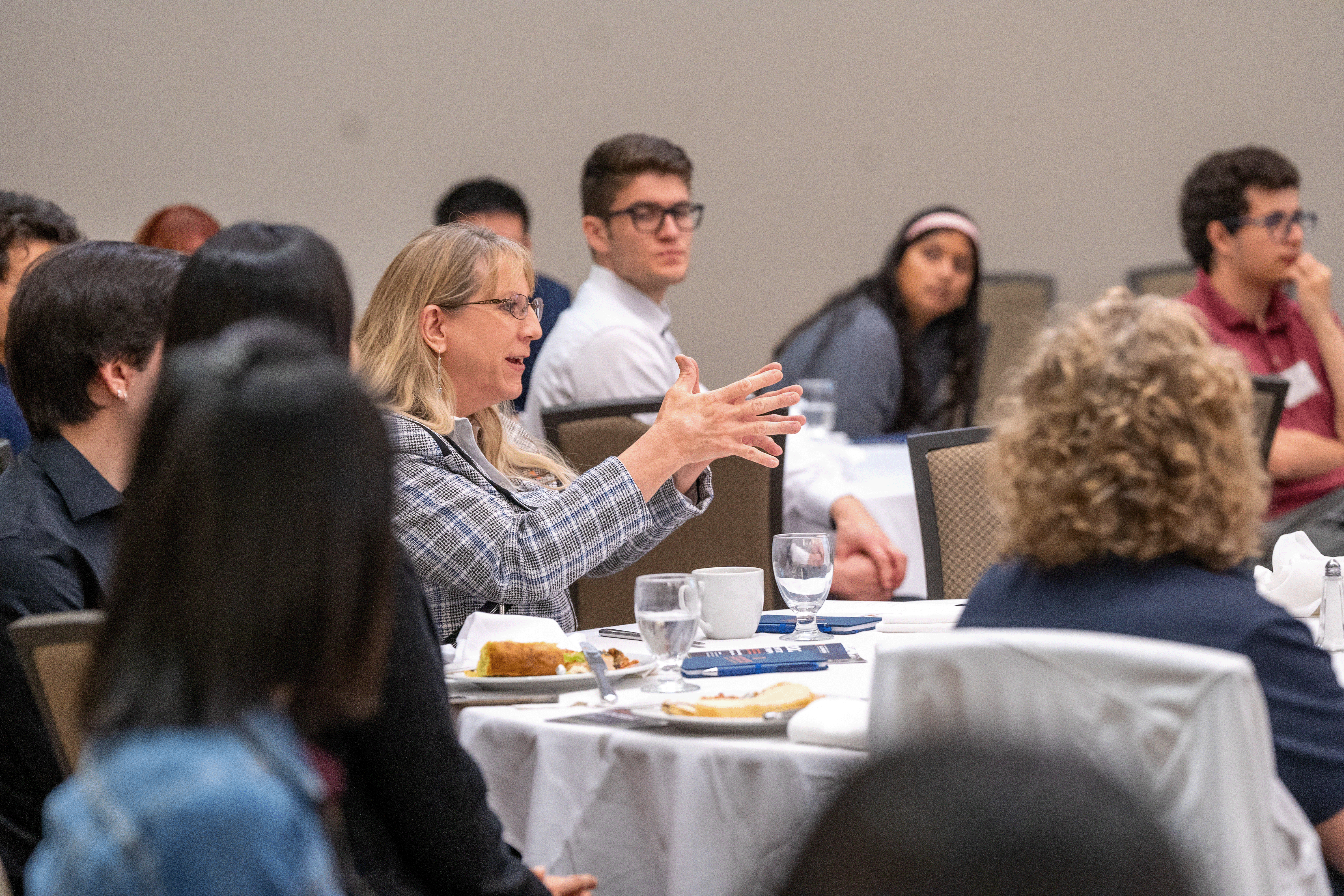 woman sitting at at table asking a question while other people around her listen