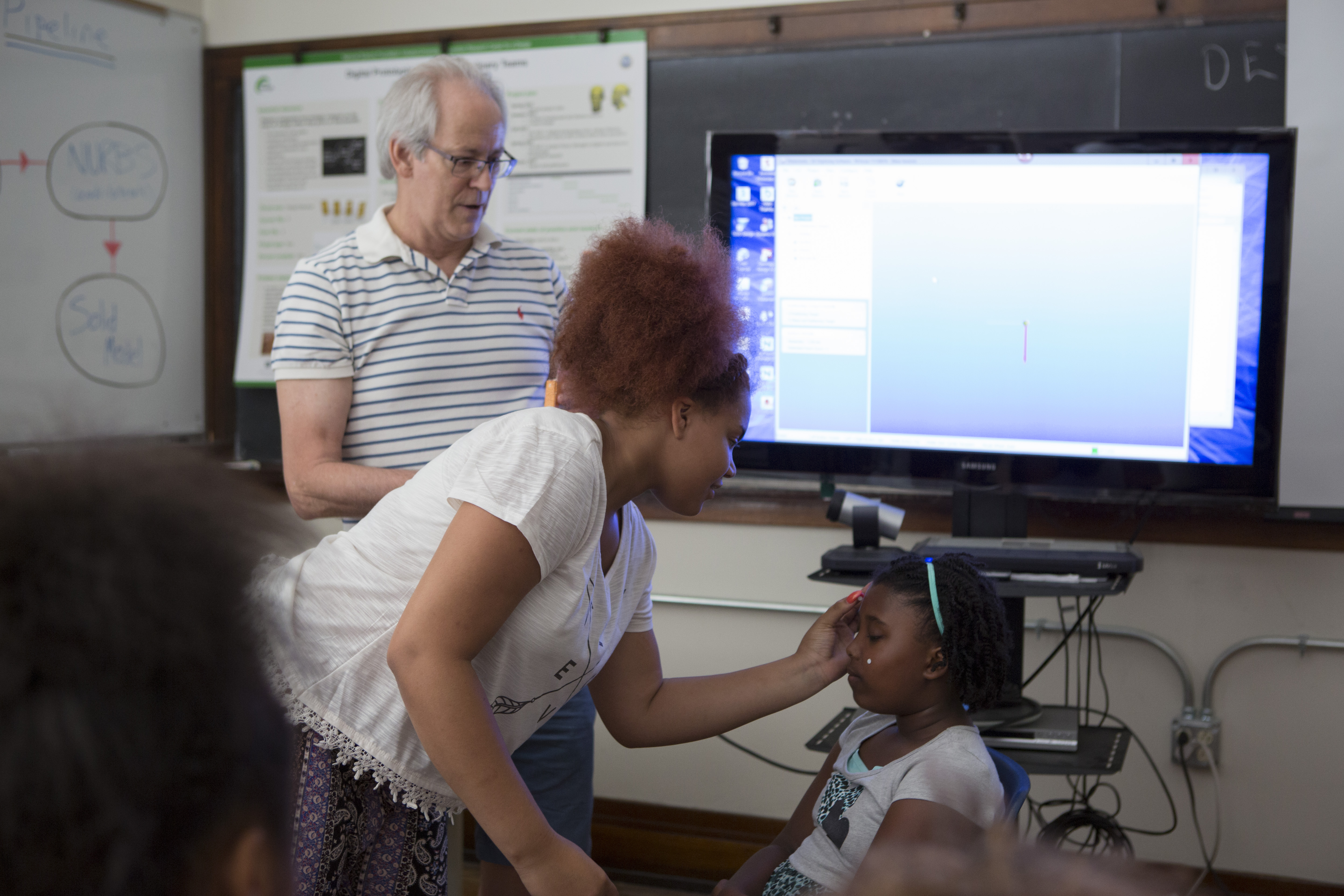 Jim Leake oversees 10th grade Taylin Martin applying reflective dots to the face of 6th grade Jamaicca Dyer. The scanner will read the locations of these dots and use them to reconstruct a 3D model of Dyer's face.